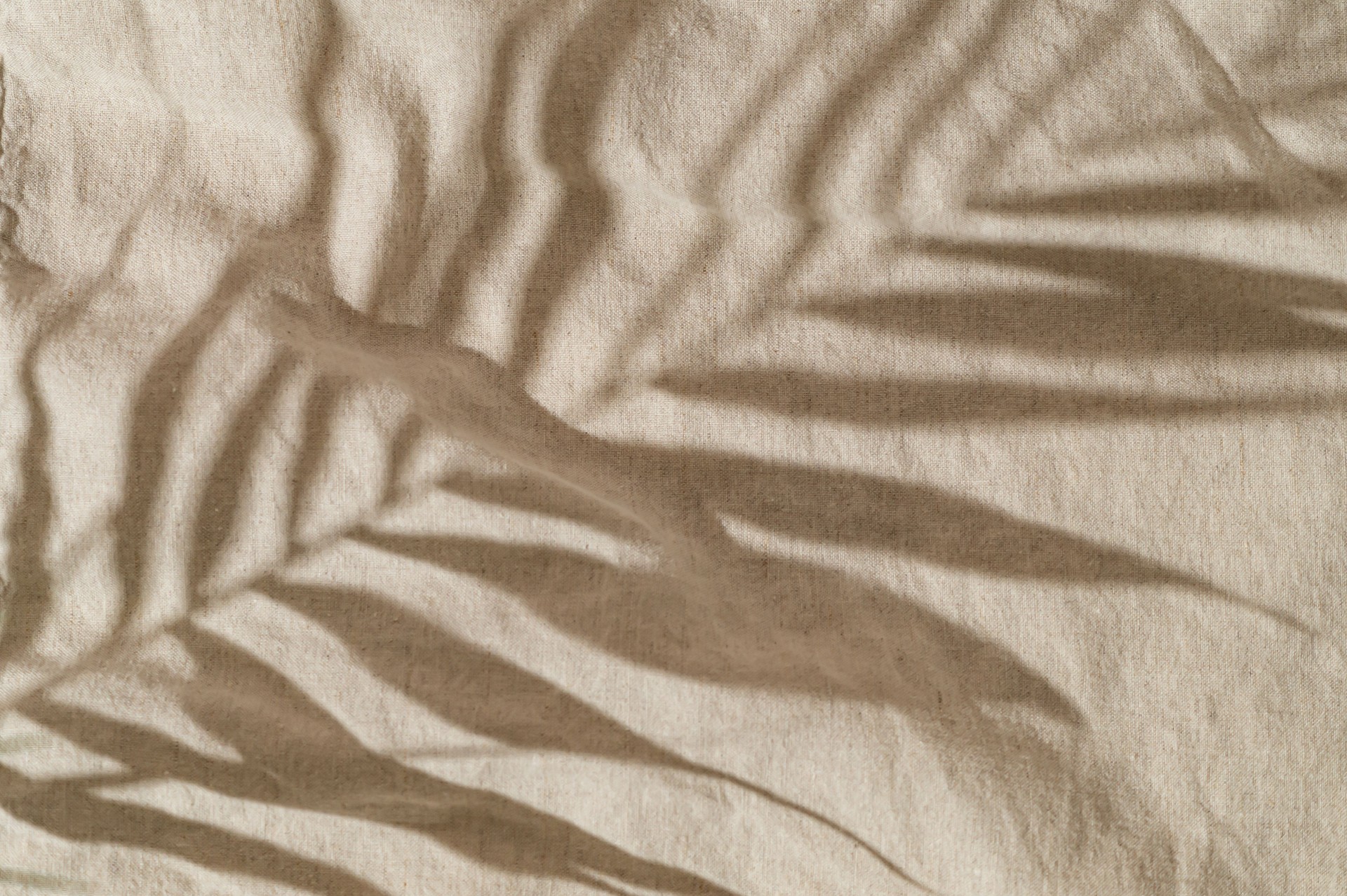 Tropical palm tree leaves shadow on sand color linen background. Minimal summer concept. An original backdrop image with a play of light and shadow. Creative copy space. Summer aesthetic. Flat lay.